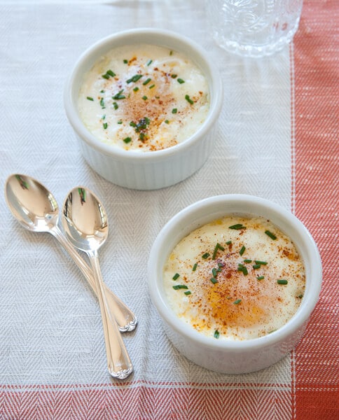 overhead shot of two ramekins of this baked egg recipe - shirred eggs. Garnished with chives and shown with tow spoons.