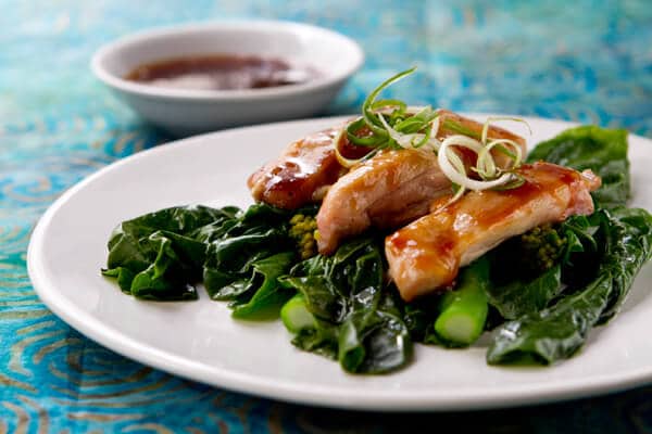 Gai lan (chinese broccoli) with tangerine glazed chicken on a white plate. 