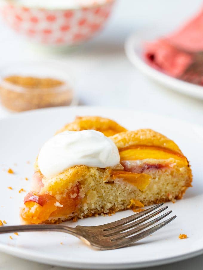 Slice of fresh fruit cake on a plate with plates and bowls in the background.