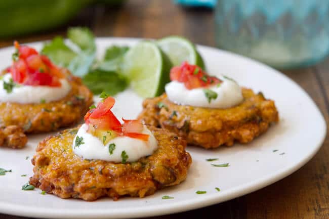 hatch chile and corn fritters on a plate garnished with sour cream and salsa.