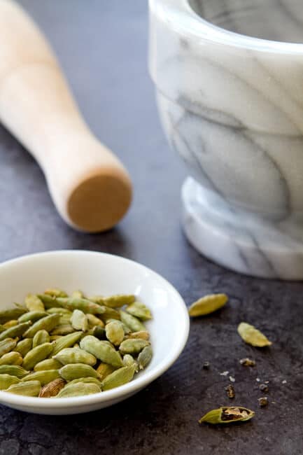 green cardamon pods with a mortar and pestle