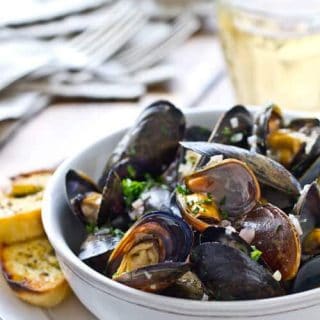 White wine mussels recipe in a bowl with a side of garlic bread.