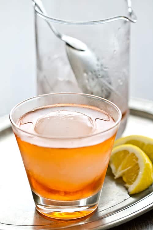 A glass of an Aperol negroni with a mixing glass in the background. 
