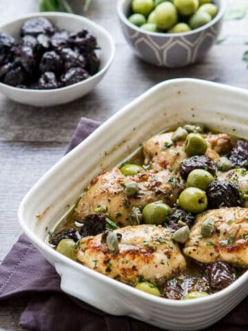 chicken marbella in a casserole dish with olives and prunes in the background.