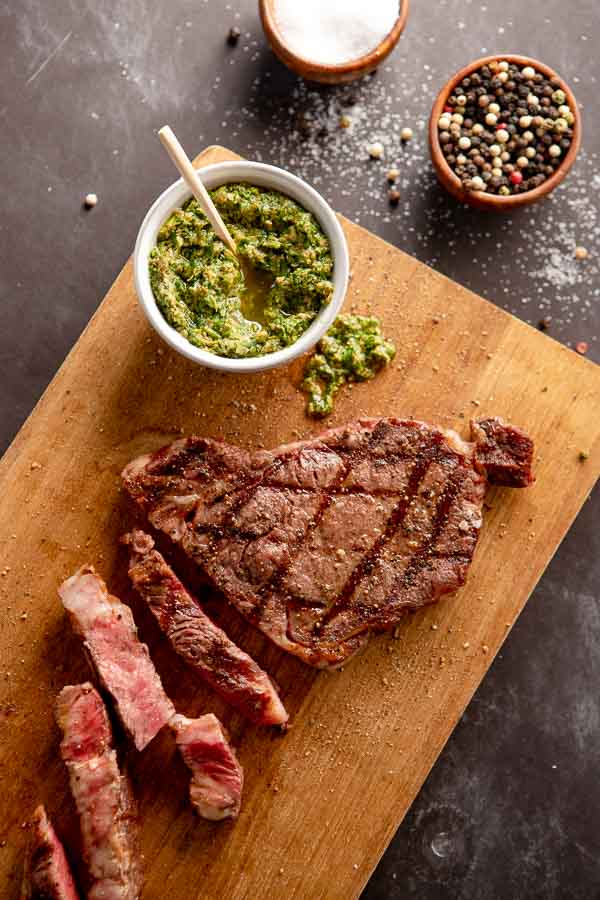 grilled ribeye steaks on a cutting board with Italian salsa verde. 