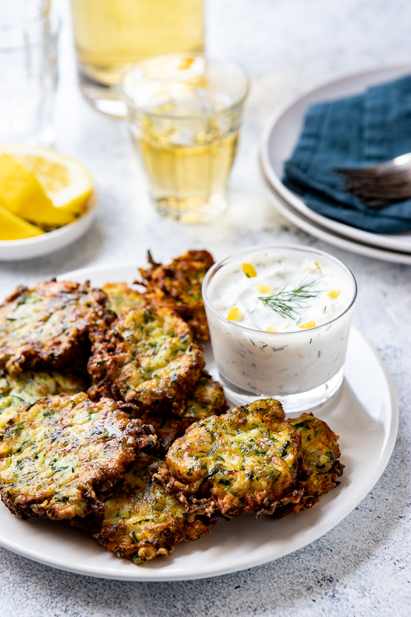 zucchini cakes on a platter with tzatziki sauce. 