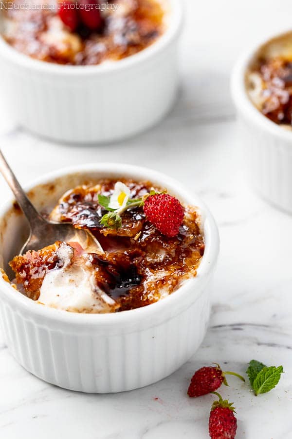 Ramekin of Strawberries and cream with a sugar crust with a spoon taking out a portion. 