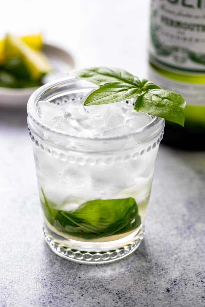 Single glass of Vermouth on the rocks with a basil leaf garnish.