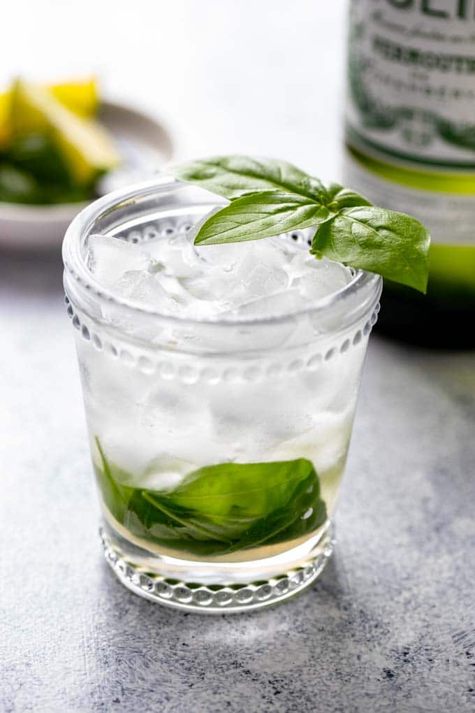 Vermouth cocktail in a glass with a basil leaf garnish.