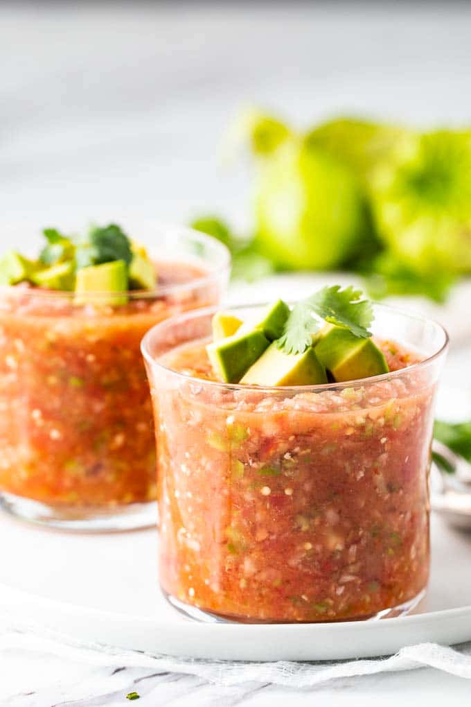 two glasses of an easy gazpacho recipe garnished with avocado and cilantro.