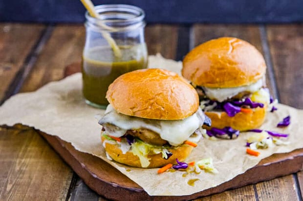up close photo of chicken sliders with green chile on parchment paper with a jar of green chile sauce in the background.