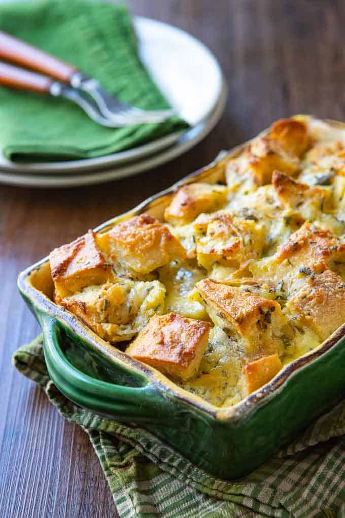 savory bread pudding recipe in a casserole dish with plates and silverware in the background.