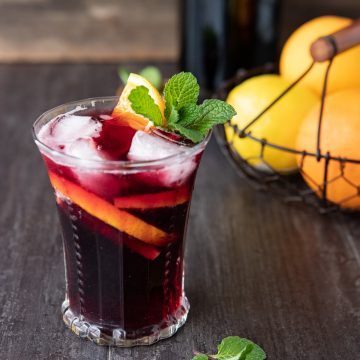 A glass of tinto de verano on a table with lemons and oranges in the background.