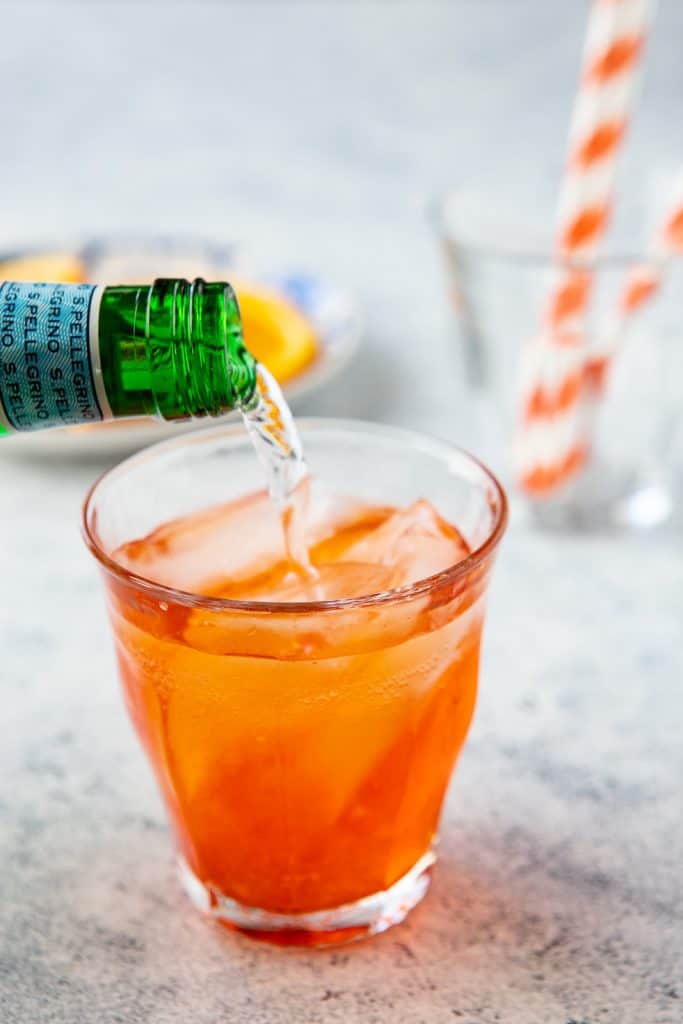 Sparkling water being poured into a glass with aperol and prosecco