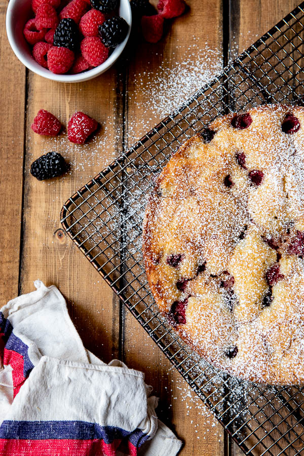 Butter cake with raspberry infused berries on a cooling rack with dusting of powdered sugar.