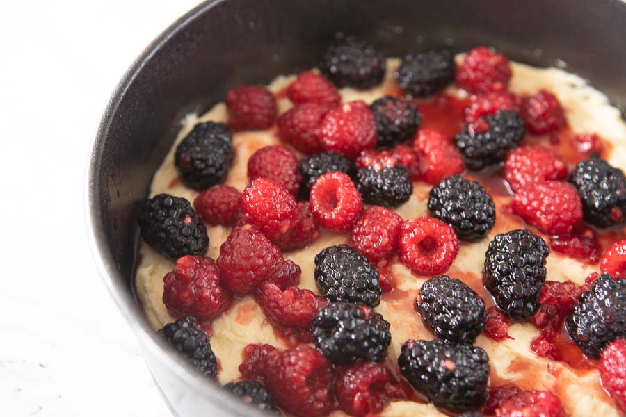 raspberry liqueur infused berries topping the butter cake batter in a springform pan. 