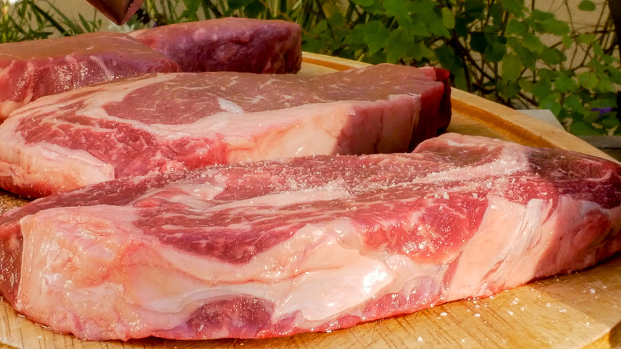 Step #1 for grilling ribeye steaks - steaks on a cutting board with salt and pepper. 