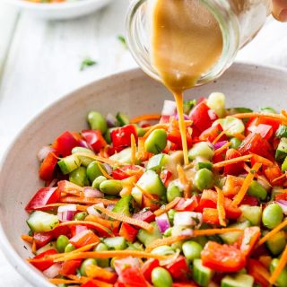 Bowl of Edamame Salad with dressing being poured on the top.