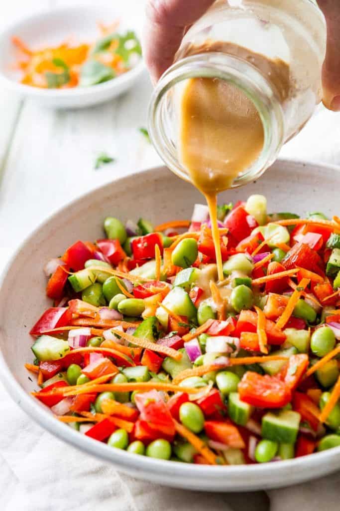 Jar of ginger vinaigrette poured over edamame salad in a bowl. 