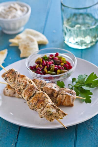 Cinnamon and cumin flavor these easy Baharat chicken skewers. With apomegranate relish, tahini yogurt sauce and pita make an exotic weeknight dinner.