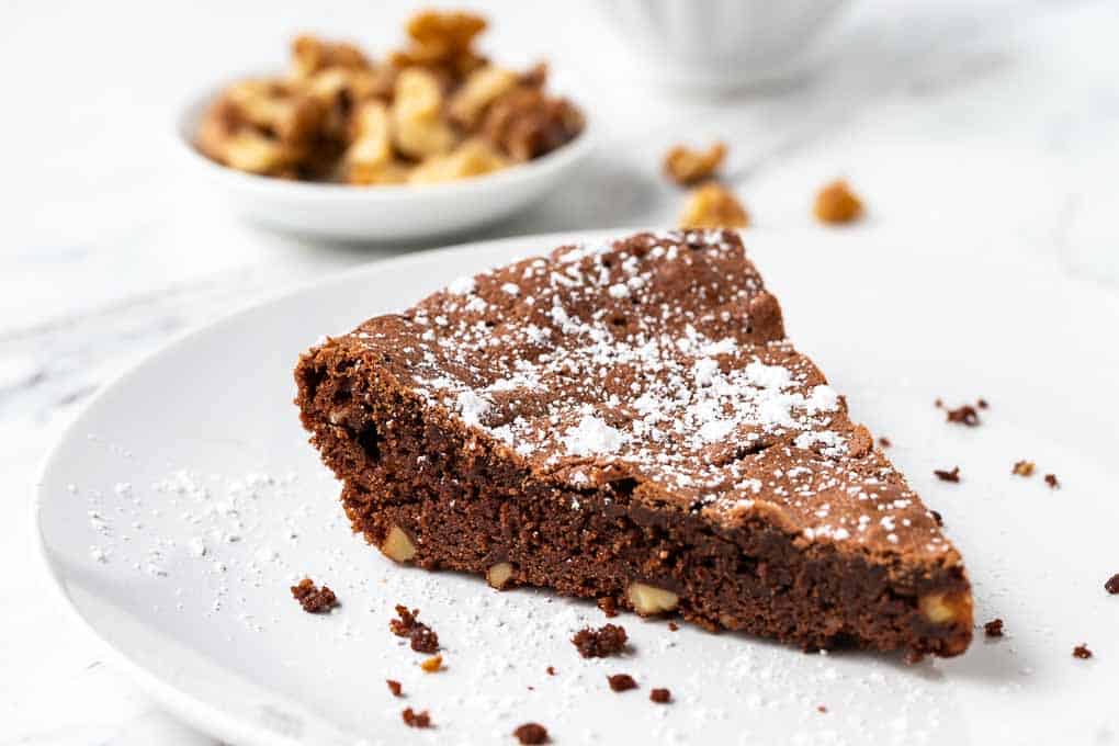 Close up of crustless brownie pie on a plate with walnuts in the background.