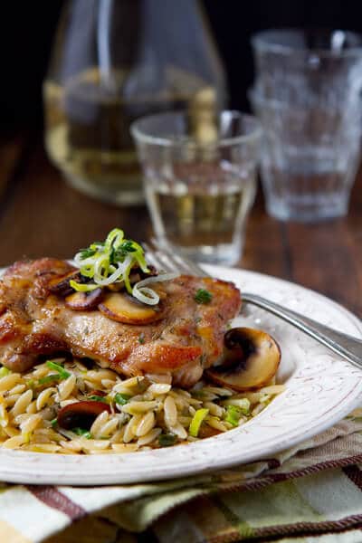 mushroom orzo risotto on a plate with a sauteed chicken thigh on top.