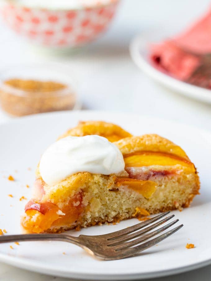 Slice of fresh fruit cake on a plate with plates and bowls in the background. 