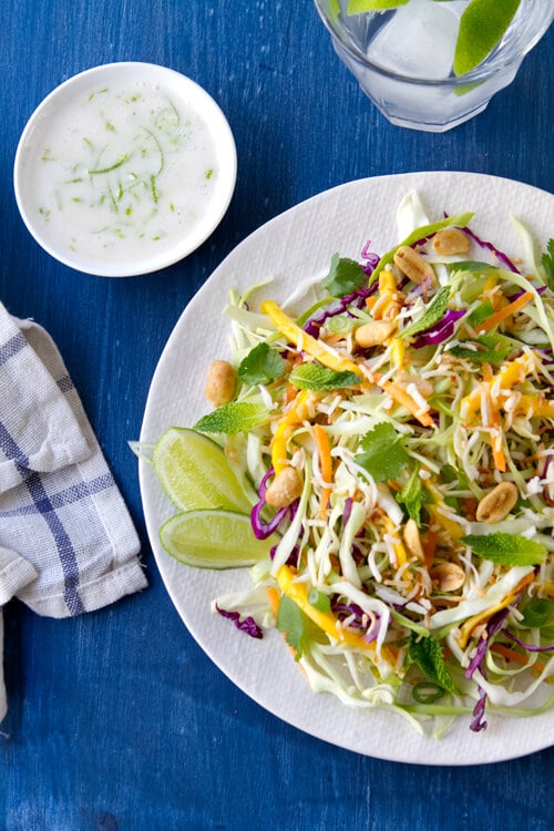 Overhead photo of no may Thai coleslaw with coconut and lime with a bowl of dressing on the side.