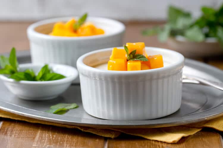 Two ramekins of the baked yogurt recipe with a bowl of fresh mint on a platter.

