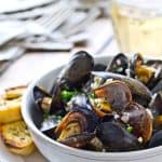 White wine mussels recipe in a bowl with a side of garlic bread.