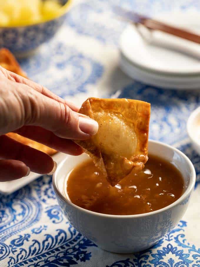dipping a crab rangoon into the sweet and sour dipping sauce.