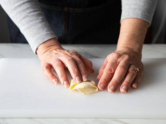 Folding the triangle corners over the center of the crab rangoon wonton wrapper.