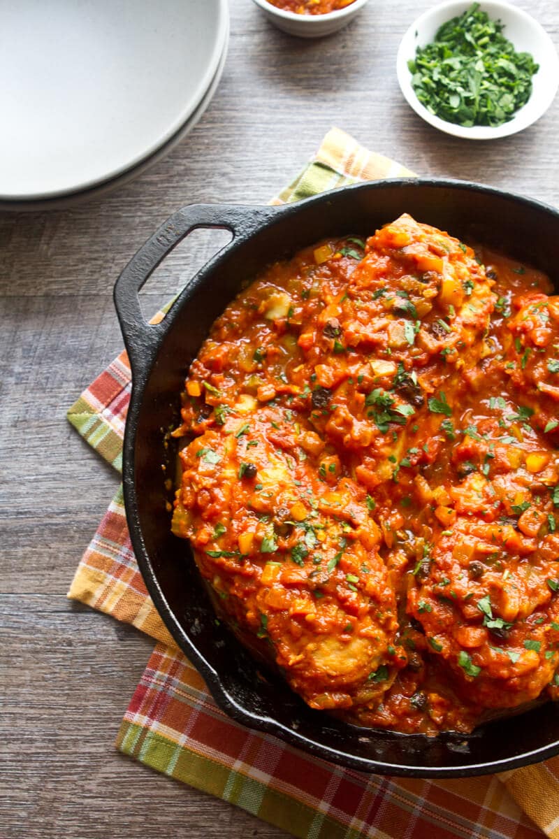 Overhead photo of this Country Captain Chicken recipe in a skillet with plates on the side. 
