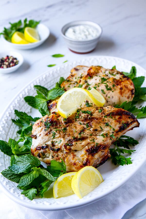 Platter of greek yogurt chicken with a side of yogurt sauce for the chicken. 

