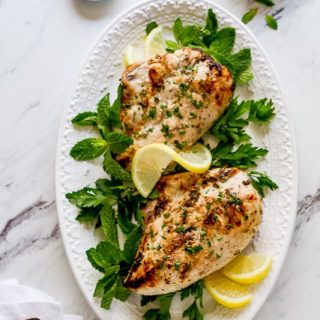 A platter of the lemon garlic greek yogurt marinated chicken with two serving spoons.