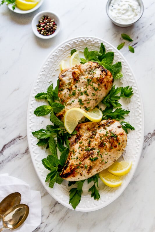 Overhead photo of greek yogurt marinated chicken on a platter with mint and lemon. 
