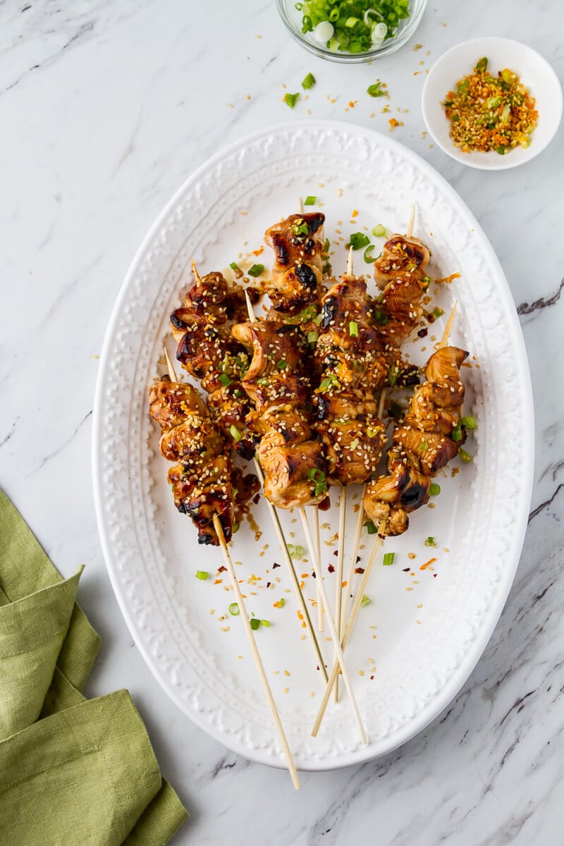 Teriyaki chicken skewers in the oven on a platter with the sesame sprinkle in a bowl to the side. 
