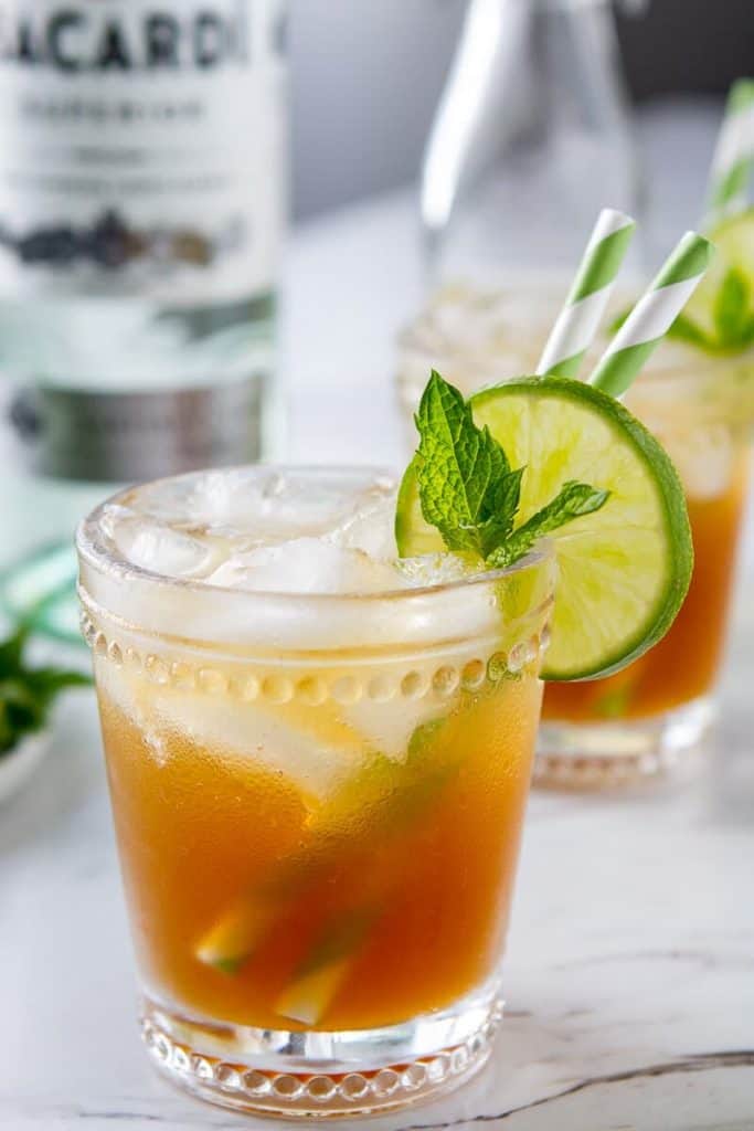 A single glass of a Rum Moscow mule, aka Rum and Ginger beer, in a rocks glass with a  mint, lime and colored straw garnish. 

