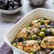 chicken marbella in a casserole dish with olives and prunes in the background.