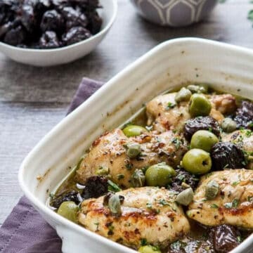 chicken marbella in a casserole dish with olives and prunes in the background.