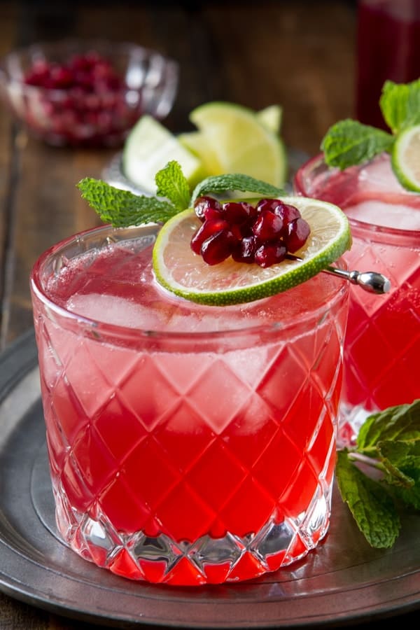 Two rocks glasses with the Fizz Cocktail and a lime, pomegranate and mint garnish.