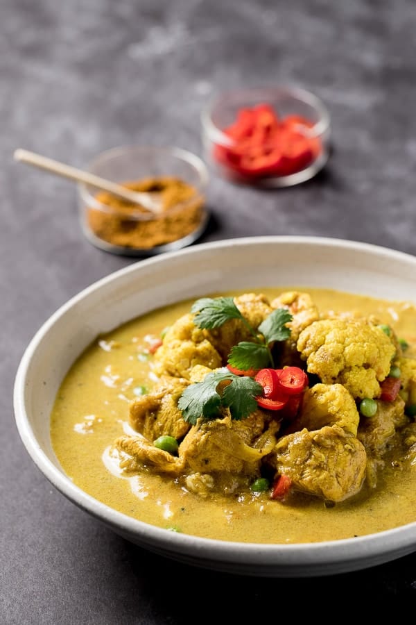 A bowl of Coconut Chicken Curry with condiments in the back. 