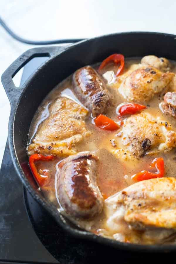 Skillet with Chicken Scarpariello with sausage simmering on the stove. 

