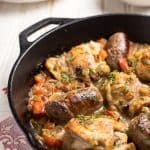 Chicken Scarpariello in a cast iron skillet with plates in the background.