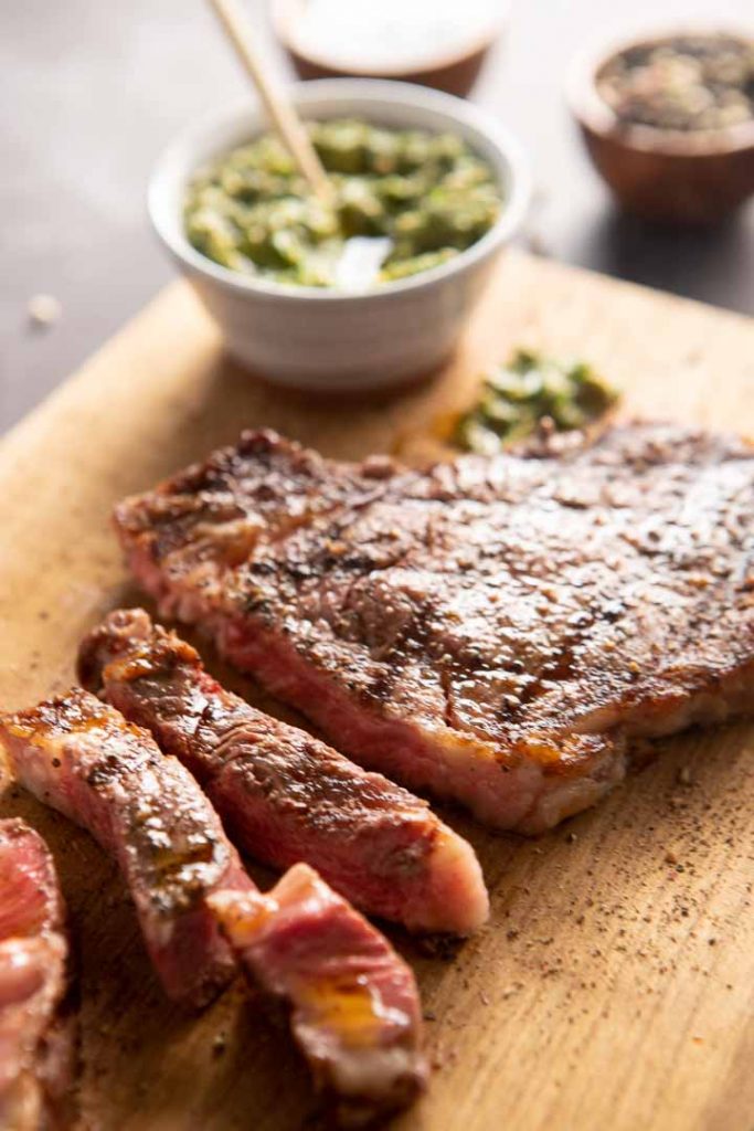 Sliced grilled ribeye steak with italian salsa verde on a cutting board. 