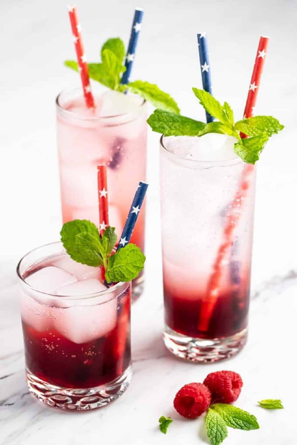 3 glasses of a vodka spritzer garnished  with straws and  mint. 