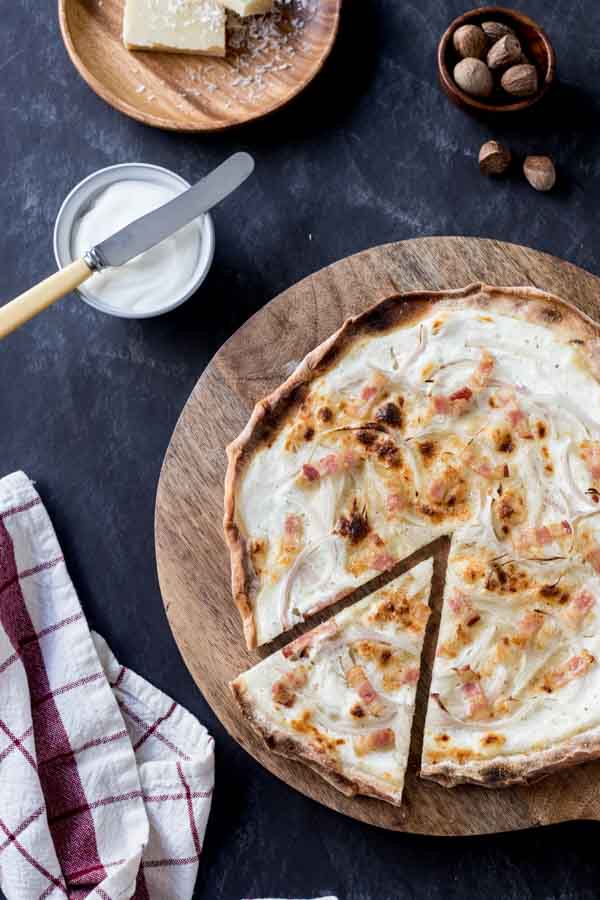 Finished Tarte Flambee on a board with cheese and sour cream.