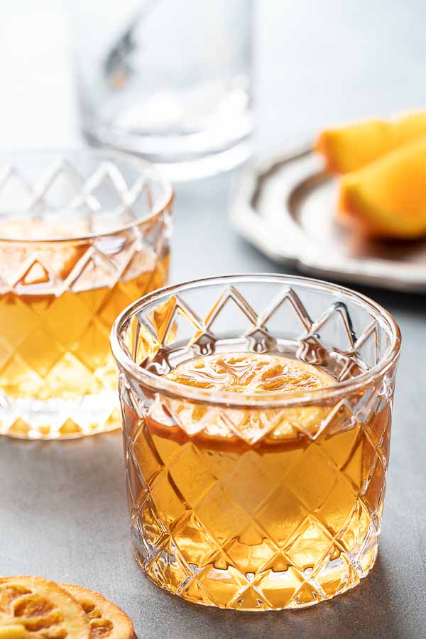 The bourbon old fashioned in two rocks glasses with an orange garnish.