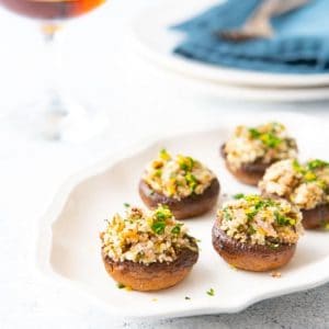 Platter of stuffed mushrooms with a glass of wine and plates in the background