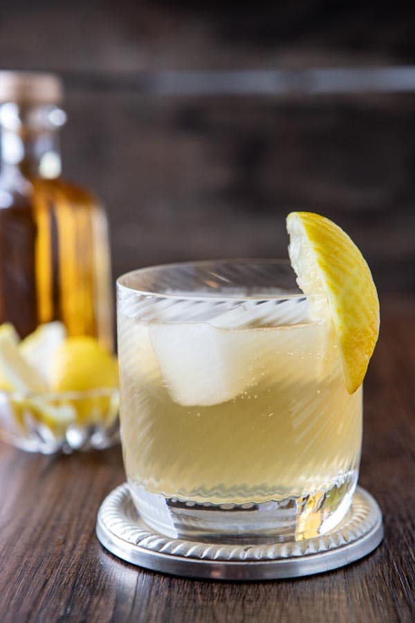 Old fashioned glass with a vanilla whiskey mule garnished with a lemon wedge. 